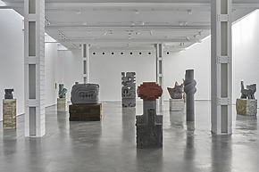 Art gallery with various abstract sculptures on display in a spacious, well-lit, modern white interior with concrete floor.