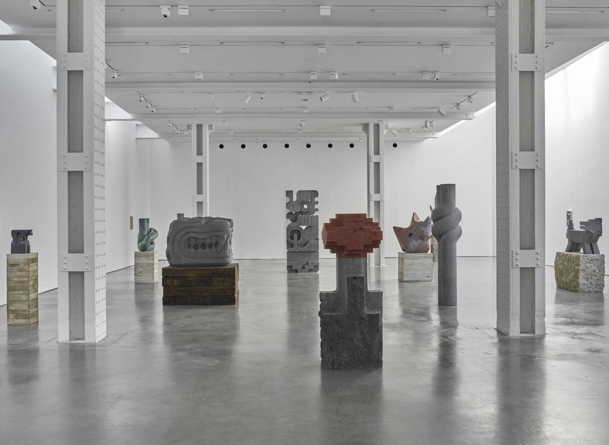 Art gallery with various abstract sculptures on display in a spacious, well-lit, modern white interior with concrete floor.