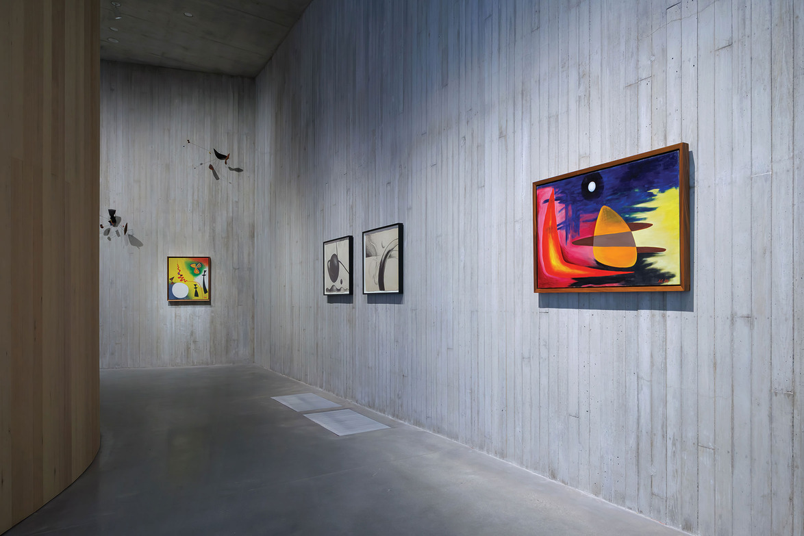 Art gallery with a concrete wall displaying a variety of colorful abstract paintings, including geometric and surreal designs.