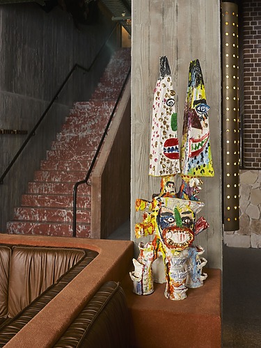Colorful abstract sculptures on a wooden surface in a modern interior with a red staircase and leather seating.