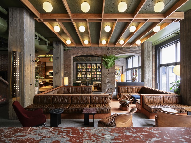 Stylish modern lobby with leather seating, round lights on a wooden ceiling, and exposed brick walls.