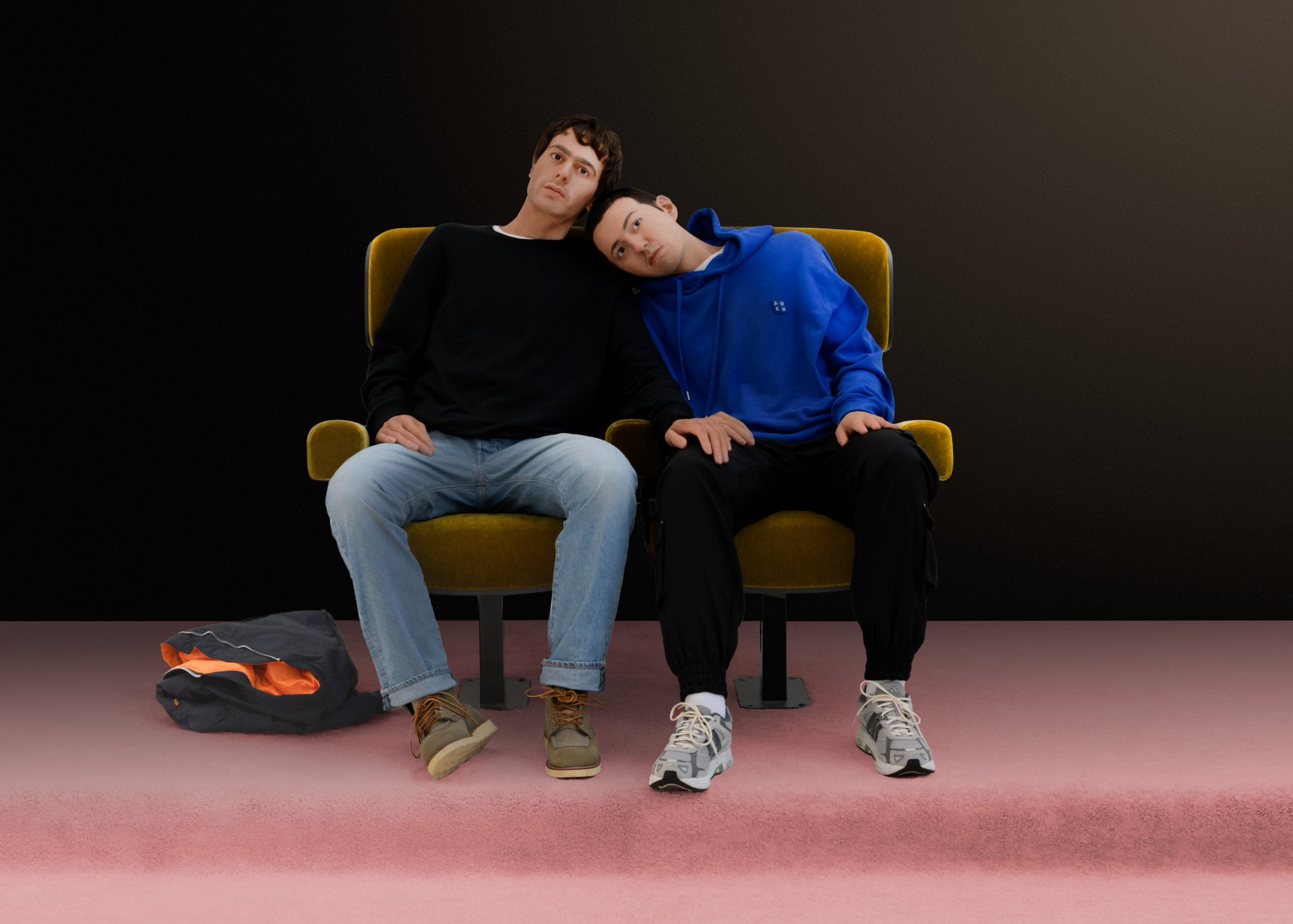 Two people sitting on theater seats, one wearing a black shirt, the other in blue, with a head resting on the other's shoulder.