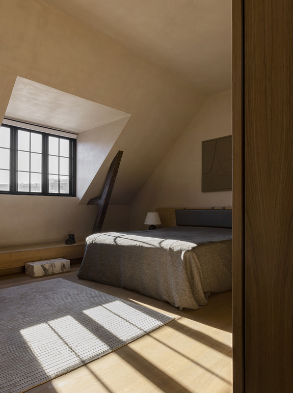 Minimalist attic bedroom with sloped ceiling, large window, neutral tones, cozy bed, and soft natural light illuminating the space.