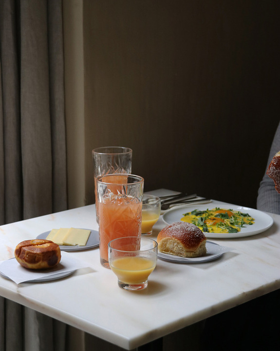 Breakfast table with croissant, juice, cheese, bread, and a plate of eggs near a window with natural light.