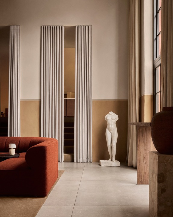 Modern interior with red sofa, white curtains, and a classical sculpture in a spacious room.