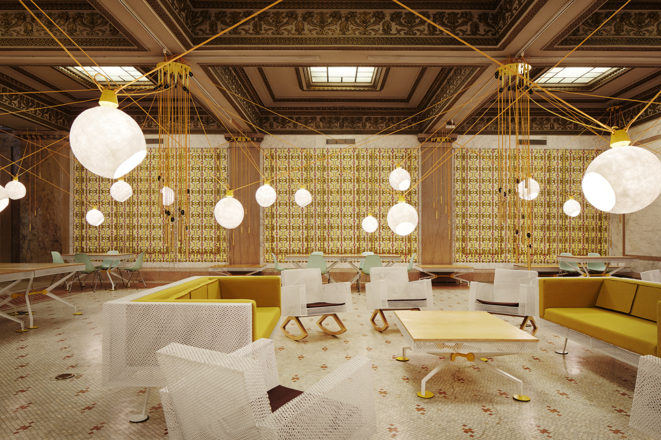 Modern restaurant interior with yellow sofas, white chairs, hanging spherical lights, and intricate ceiling and wall designs.