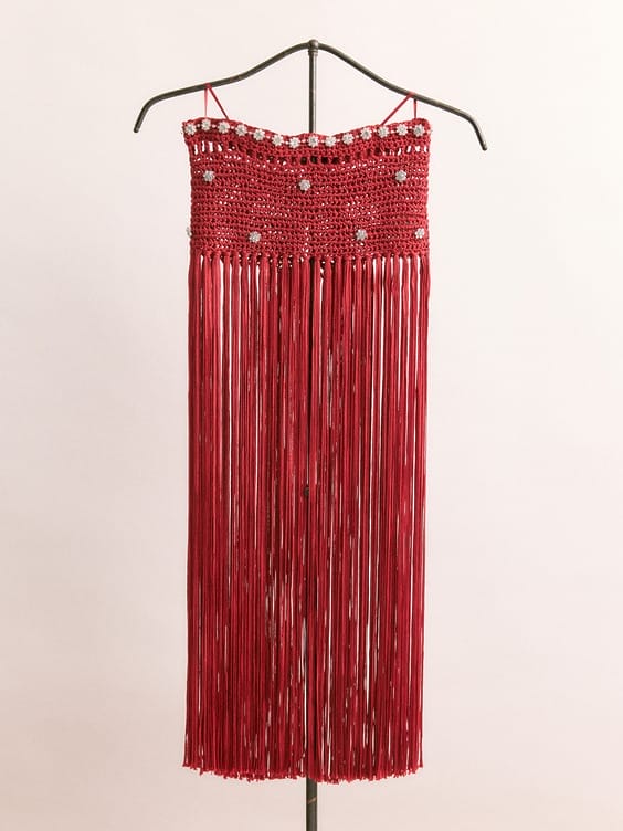 Red fringed dress on a hanger with decorative gems and intricate crochet detailing at the top.