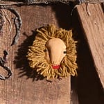 Handcrafted wooden lion face with a yarn mane mounted on a rustic wooden surface.