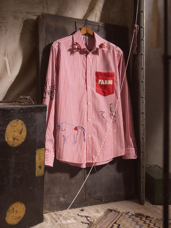 Red and white striped shirt with embroidery details and a patch reading "Fann" hanging on a rustic wooden door.