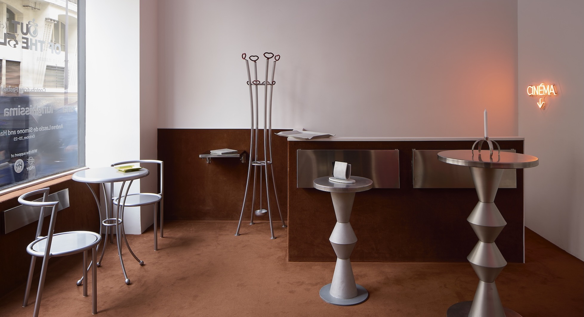 Modern café interior with unique geometric furniture, small tables, and a neon sign on a warm-toned carpeted floor.
