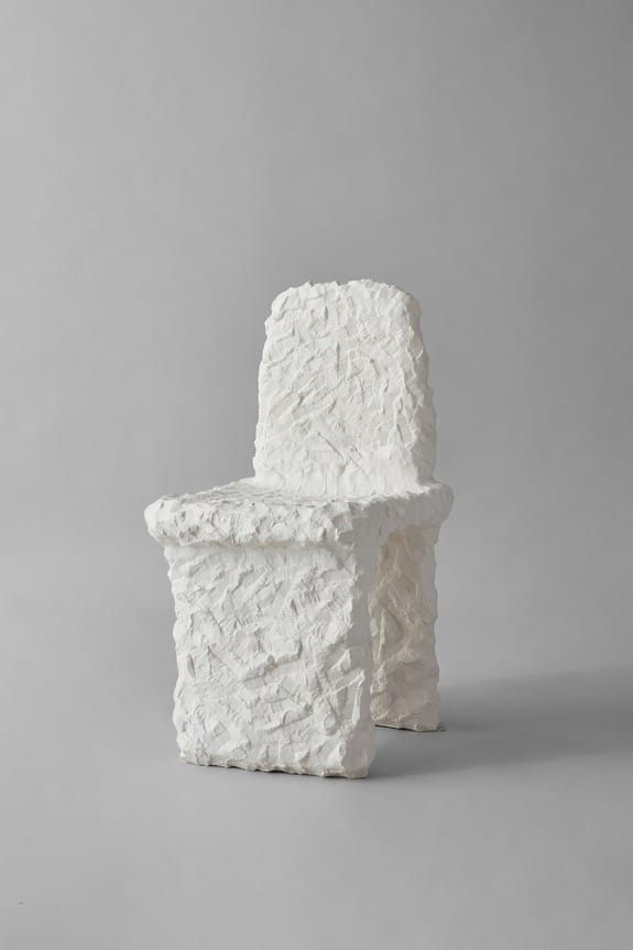 Textured white chair with a sculptural design against a plain gray background.