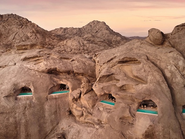 Luxury resort built into a rocky mountain landscape at sunset with unique architectural features and a dramatic sky.