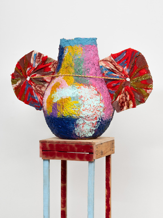 Colorful abstract vase on a wooden stand with two red and white fan-like projections on the sides.