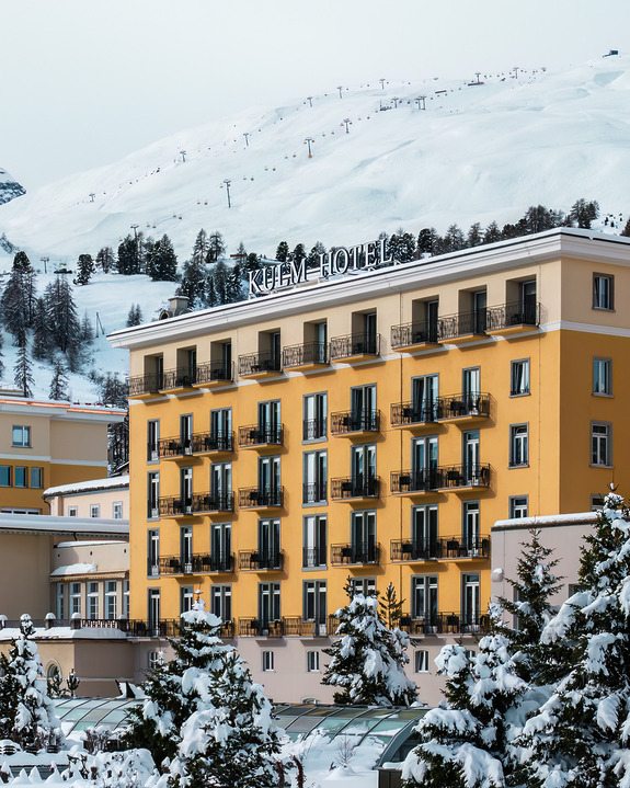 Historic alpine hotel with snow-covered landscape and ski lift in the background.