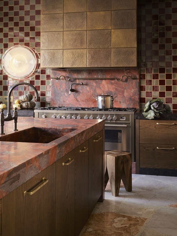 Luxury kitchen with marble countertops, wooden cabinets, large stove, tiled walls, and unique lighting fixtures.