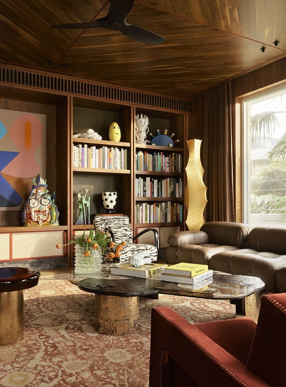 Modern living room with a bookshelf, abstract art, patterned armchair, round coffee table, and elegant rug.