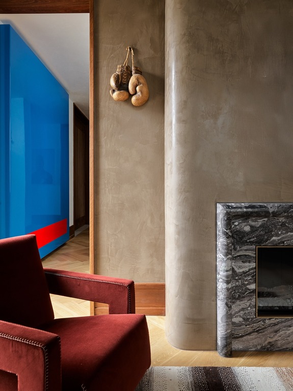 Luxurious modern interior with a red armchair, textured walls, fireplace, and boxing gloves as decor.