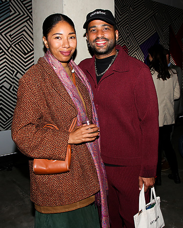 Smiling couple posing together at an indoor event with geometric patterned wall in the background.