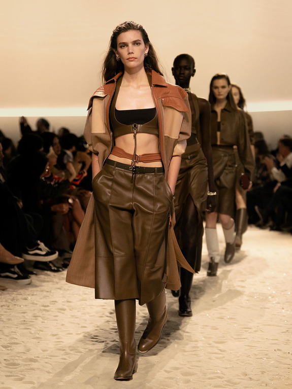 Models walking down the runway in stylish brown and beige outfits during a fashion show.