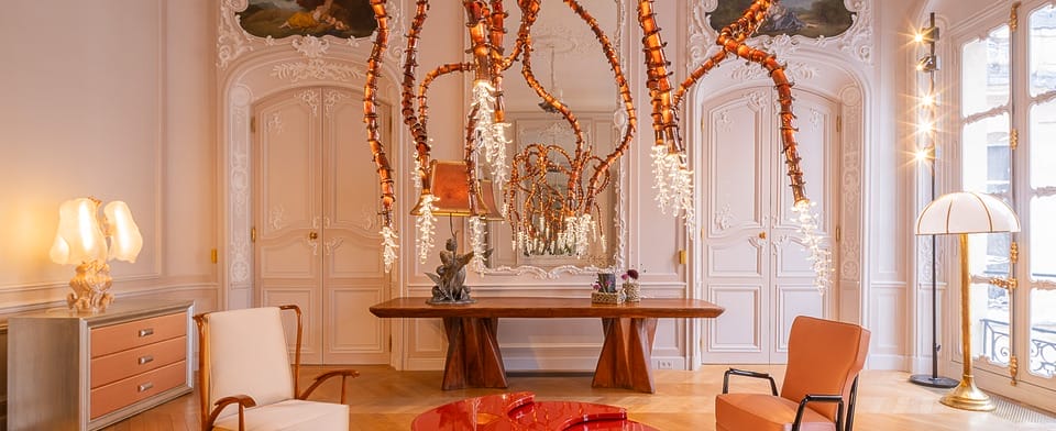 Elegant living room with ornate white walls, unique red-orange hanging light fixture, modern red tables, and stylish chairs.