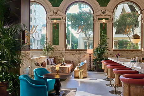 Elegant hotel lounge with plush seating, marble accents, and large arched windows offering a view of trees and city buildings.