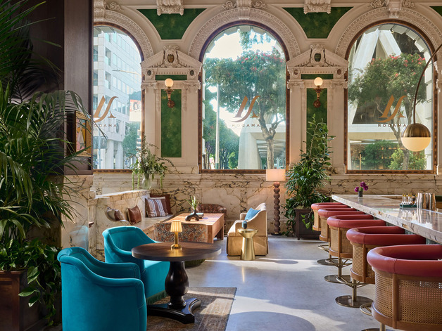 Elegant hotel lounge with plush seating, marble accents, and large arched windows offering a view of trees and city buildings.