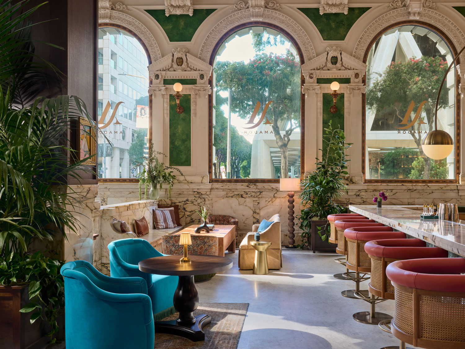 Elegant hotel lounge with plush seating, marble accents, and large arched windows offering a view of trees and city buildings.