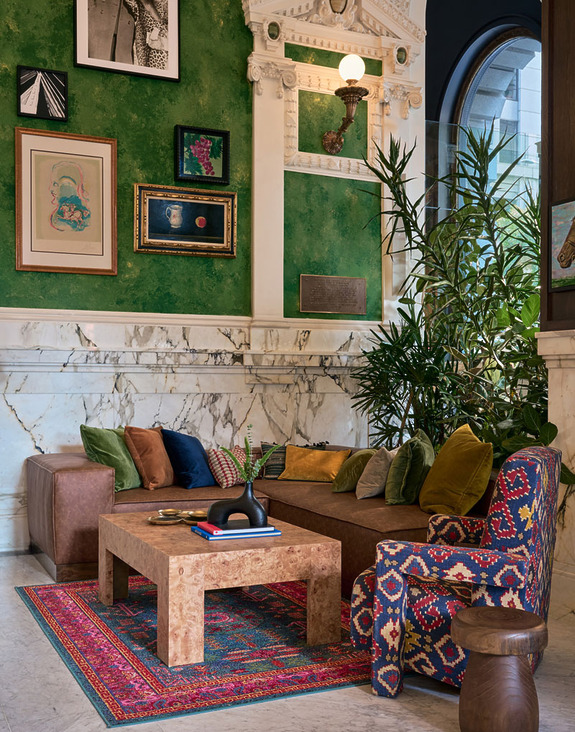 Colorful and stylish living room with a patterned rug, green walls, framed art, and a cozy seating area with various cushions.