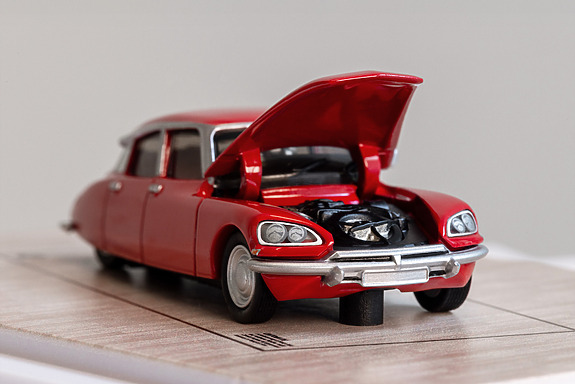 Red model car with hood open, showcasing detailed engine, displayed on a wooden base.