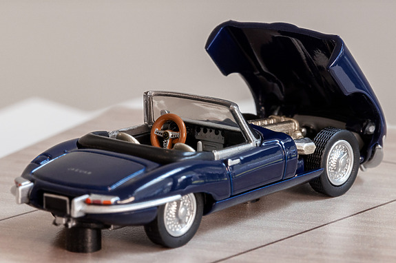 Blue vintage convertible car model with open hood on a wooden surface.