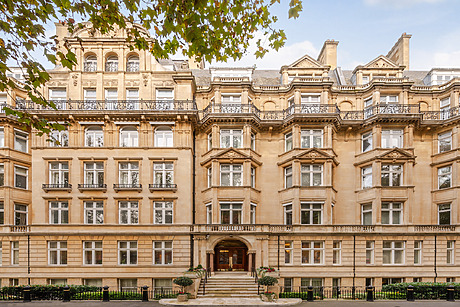 Historic stone building with ornate balconies, large windows, and arched entrance surrounded by trees on a clear day.