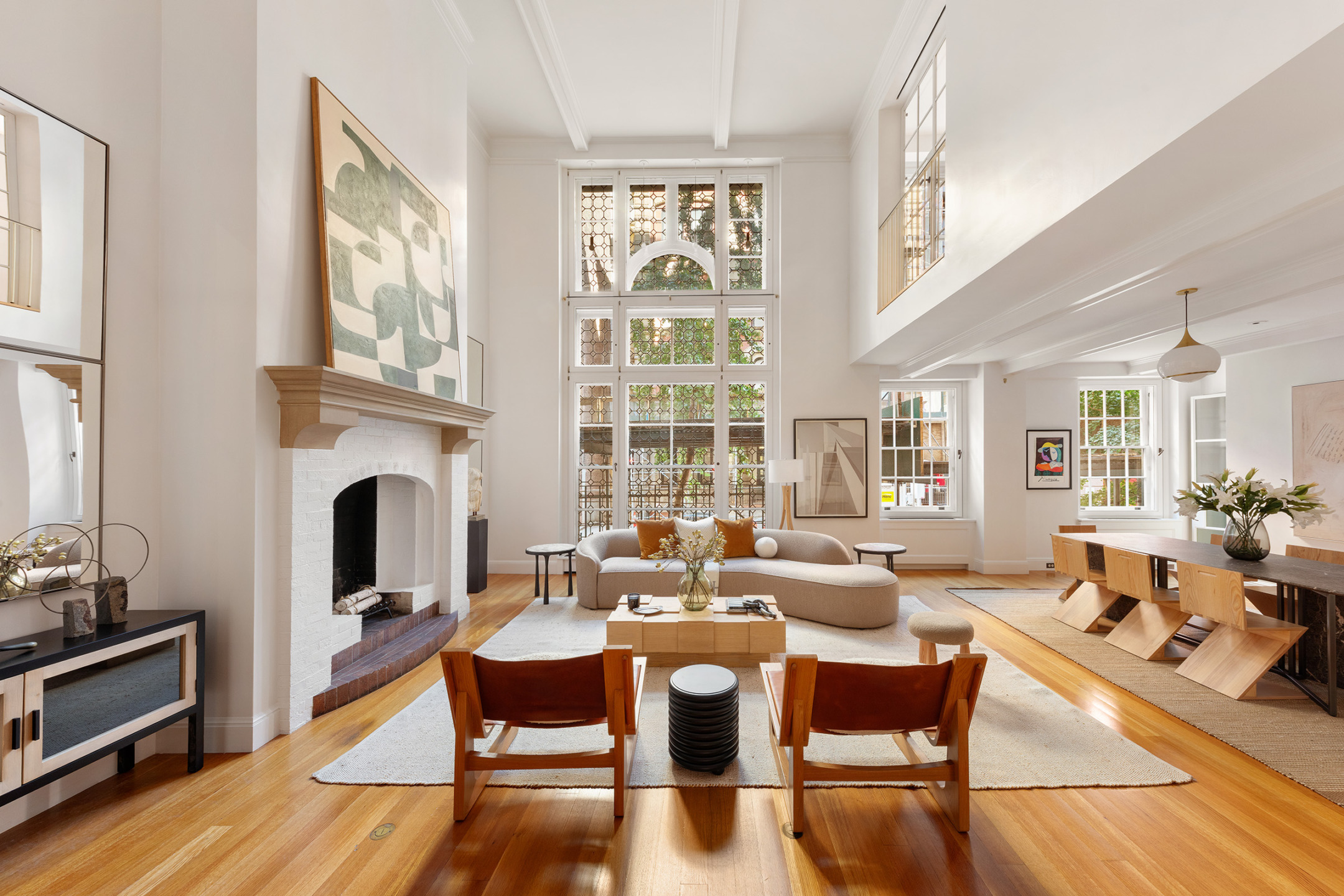 Spacious living room with high ceilings, modern furniture, large windows, and wooden floors, creating a bright and airy atmosphere.