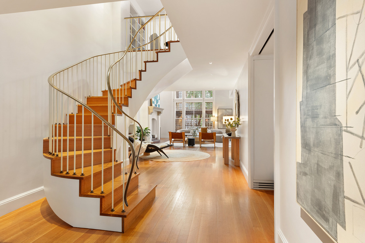 Spiral wooden staircase in modern home interior with large windows and stylish furniture in a bright, airy living space.