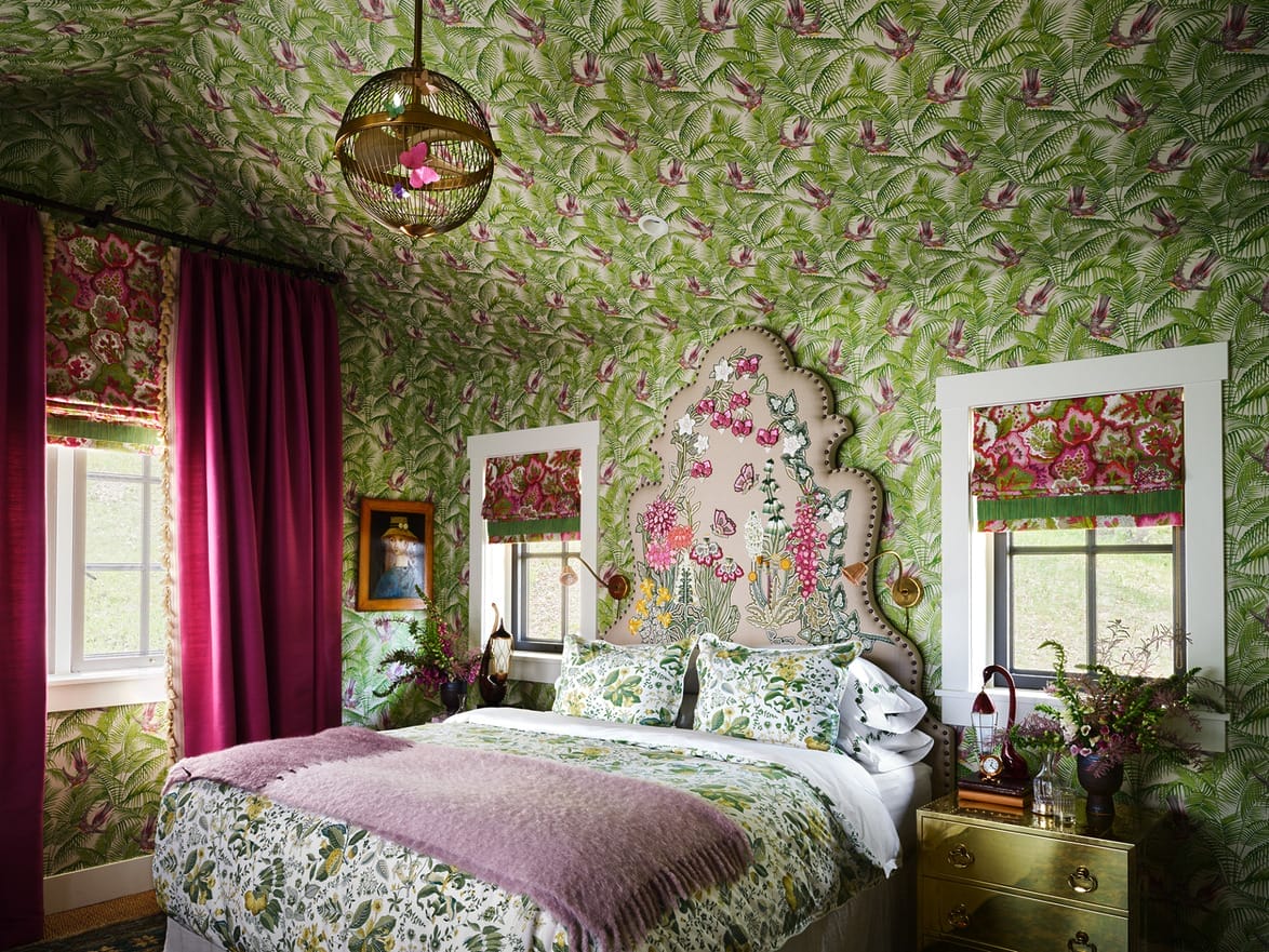 Colorful bedroom with floral wallpaper, ornate headboard, green and pink decor, pendant light, and large windows.