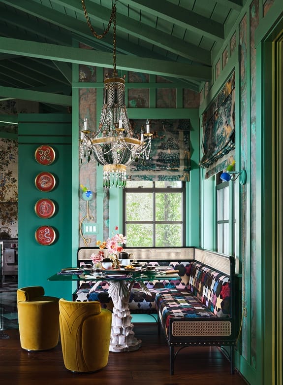 Eclectic dining area with colorful seating, decorative chandelier, and vibrant green walls adorned with plates and patterns.