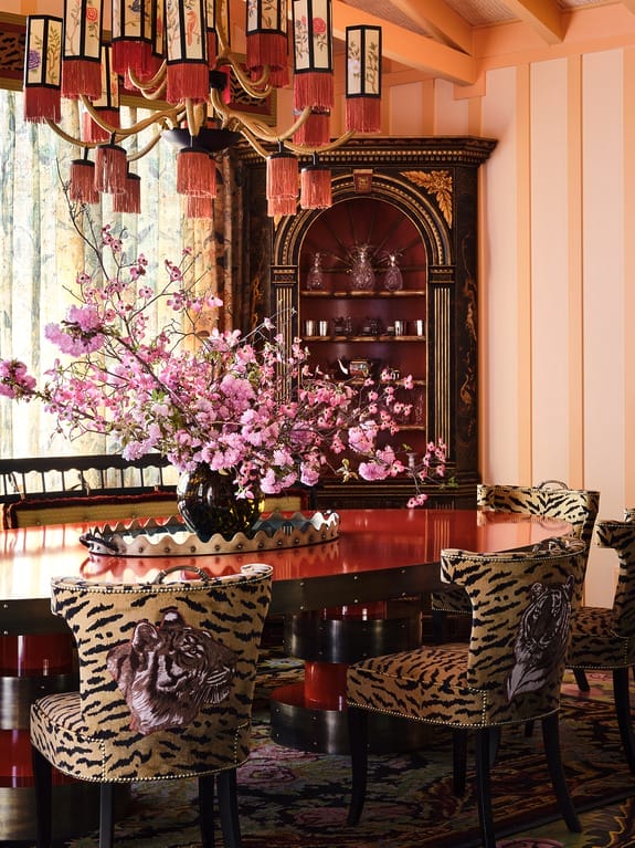 Luxurious dining room with pink floral centerpiece, tiger-patterned chairs, ornate chandelier, and intricate cabinet.