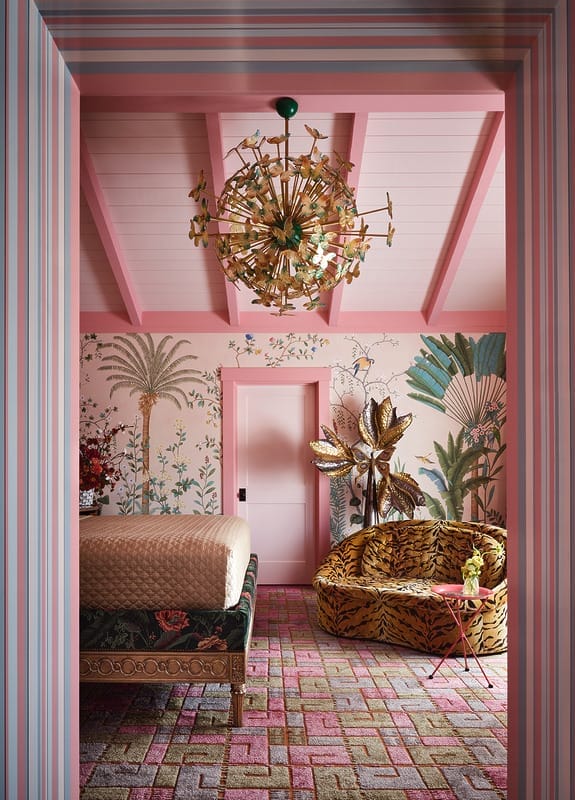 Colorful room with pink walls, vibrant floral wallpaper, a decorative bed, patterned sofa, and a large modern chandelier.