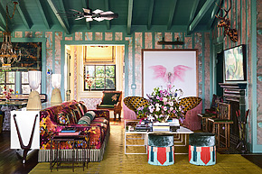 Eclectic living room with colorful furniture, floral arrangements, butterfly art, chandelier, and exposed wood ceiling beams.