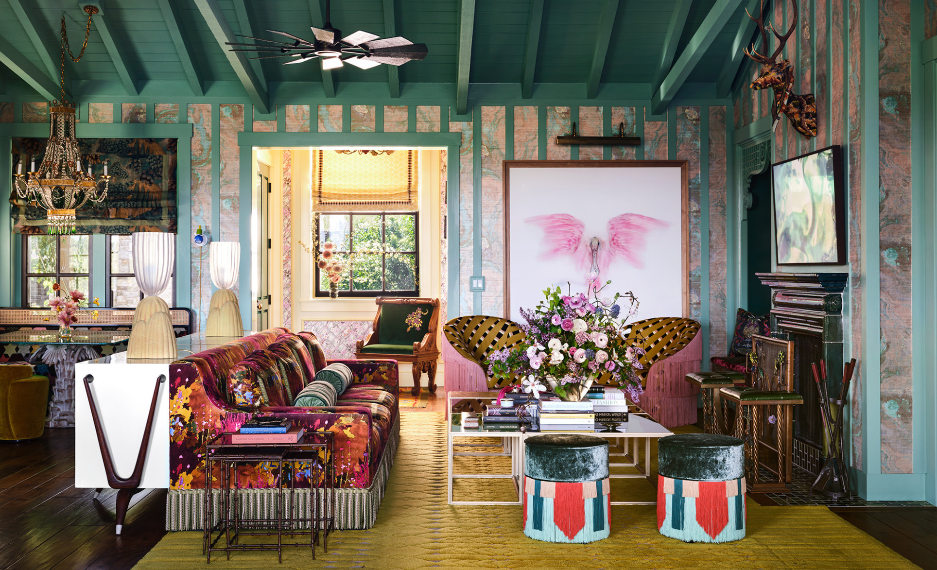 Eclectic living room with colorful furniture, floral arrangements, butterfly art, chandelier, and exposed wood ceiling beams.
