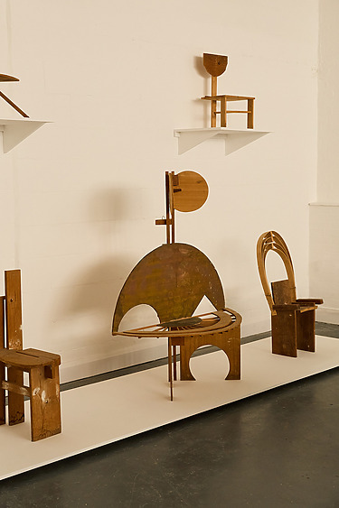Modern abstract wooden chairs displayed in an art gallery setting with a white wall background.