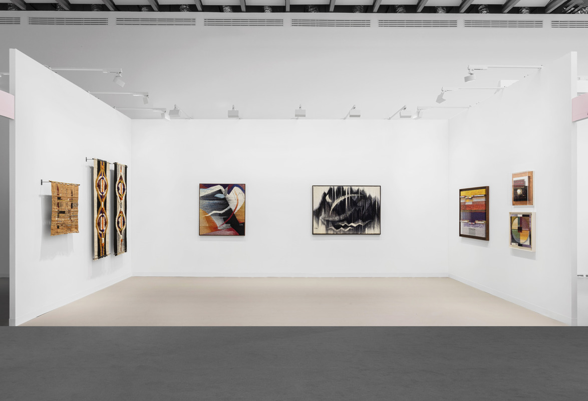 Gallery exhibition with modern art paintings displayed on white walls and overhead lighting.