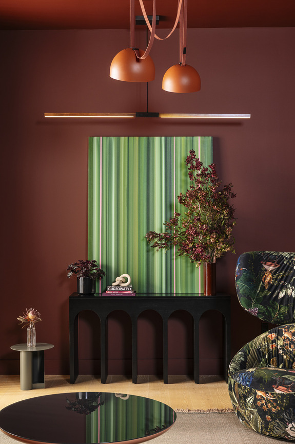 Modern interior with green striped artwork, decorative plants, round coffee table, and floral patterned sofa under pendant lights.