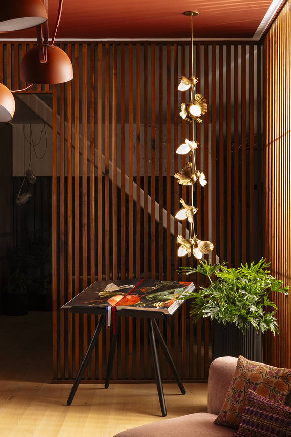 Modern interior with wood paneling, abstract table, vibrant plant, and artistic hanging light fixture. Warm and inviting ambiance.