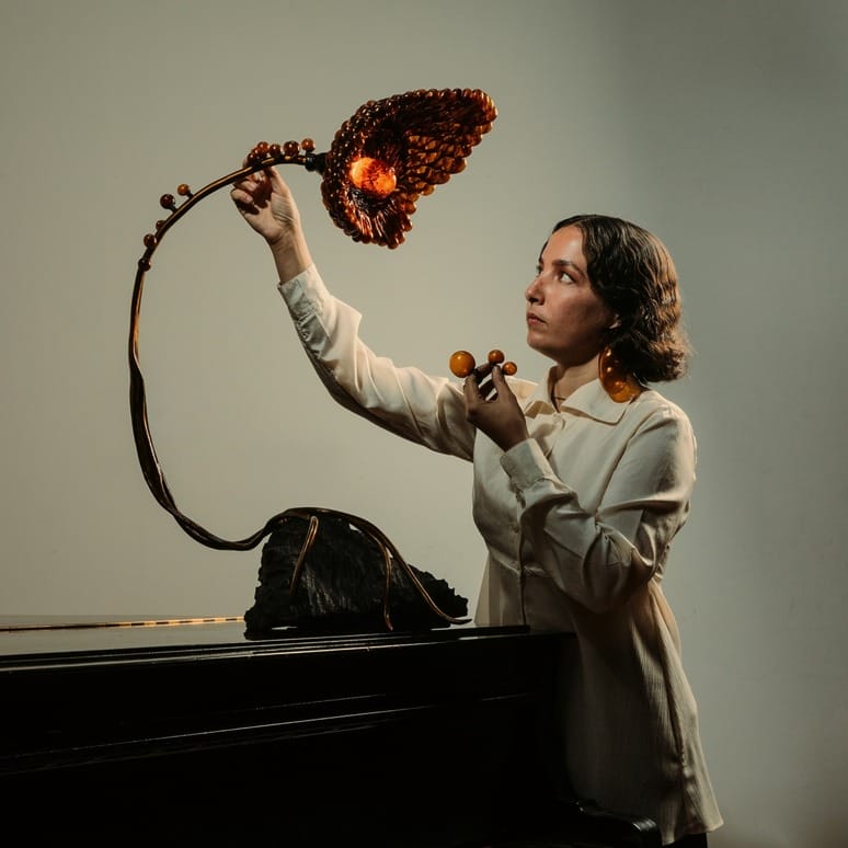 Person adjusting an artistic lamp with a floral design on a dark background.