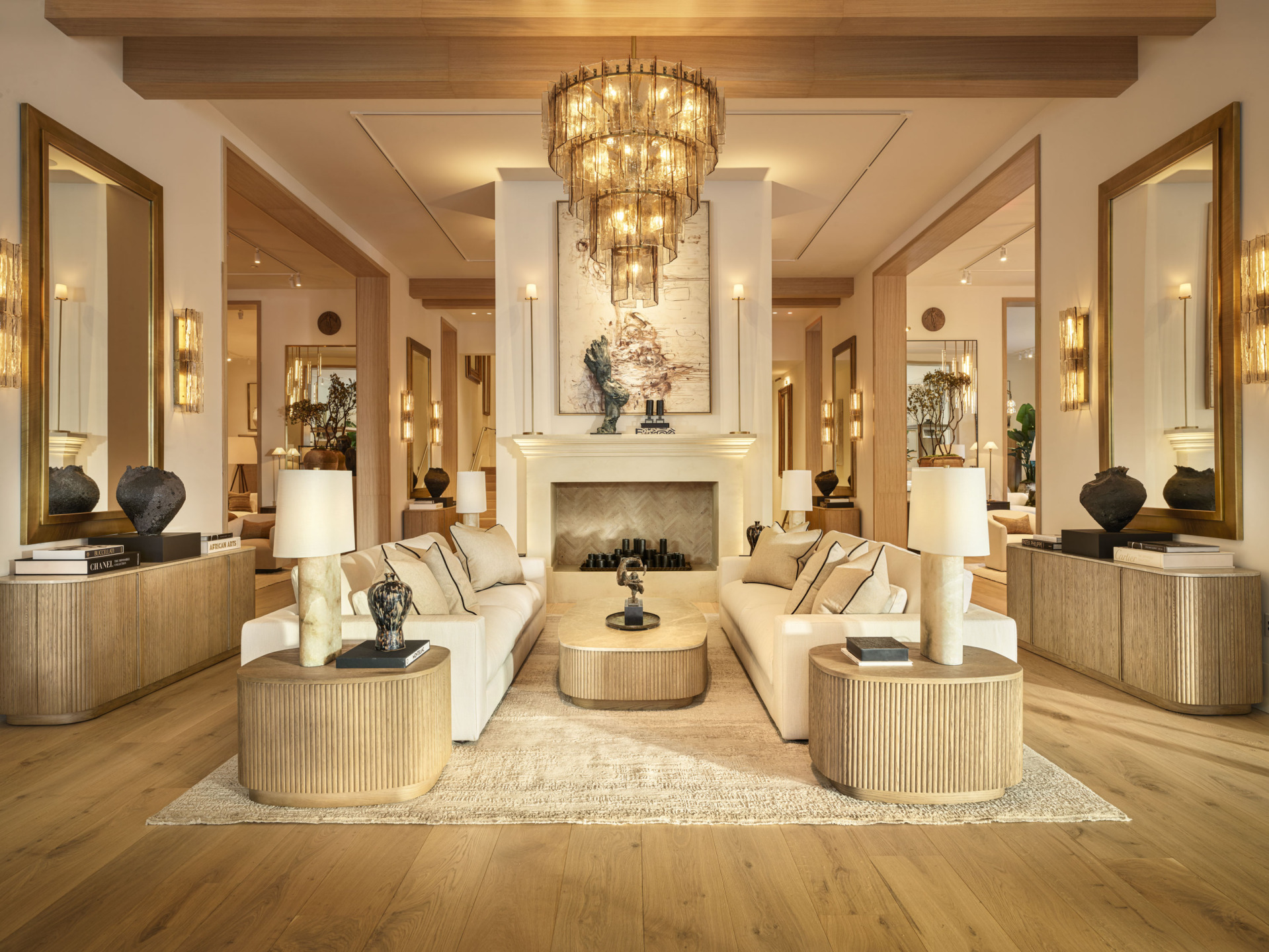 Elegant living room with beige sofas, large chandelier, modern fireplace, and wooden accents, creating a warm and inviting space.