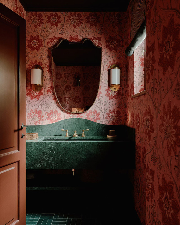 Elegant bathroom with red floral wallpaper, green marble sink, oval mirror, and stylish lighting fixtures.