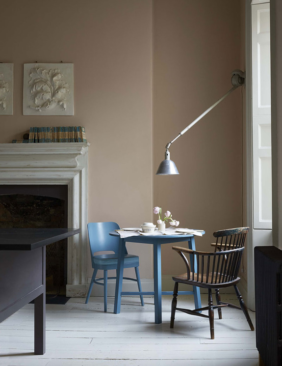 Cozy dining nook with blue and wooden chairs, small round table, and wall-mounted lamp by a fireplace in a softly lit room.