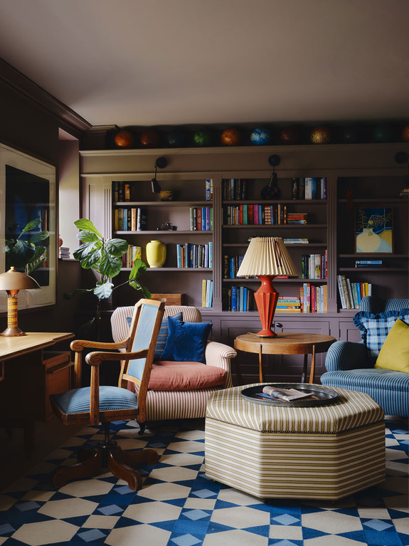 Cozy living room with colorful armchairs, a patterned ottoman, bookshelves, and eclectic decor.