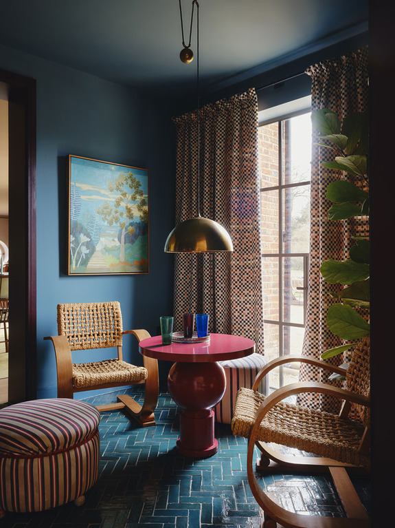 Cozy room with colorful decor, blue walls, patterned curtains, round table, wicker chairs, and a large window.