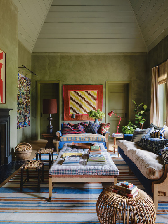 Cozy living room with colorful artwork, striped rugs, wooden coffee tables, and potted plants creating a warm atmosphere.